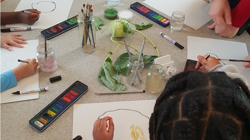 En kålrabbi ligger mitt på ett bord. Flera barn målar av kålrabbin med vattenfärger.